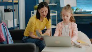 mother-daughter-reading-book-together-doing-homework-home-schoolgirl-receiving-hep-from-parent-with-online-courses-tasks-remote-education-adult-helping-child